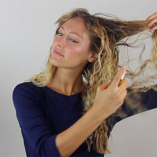 Woman spraying rahua enchanted island salt spray on her wavy hair