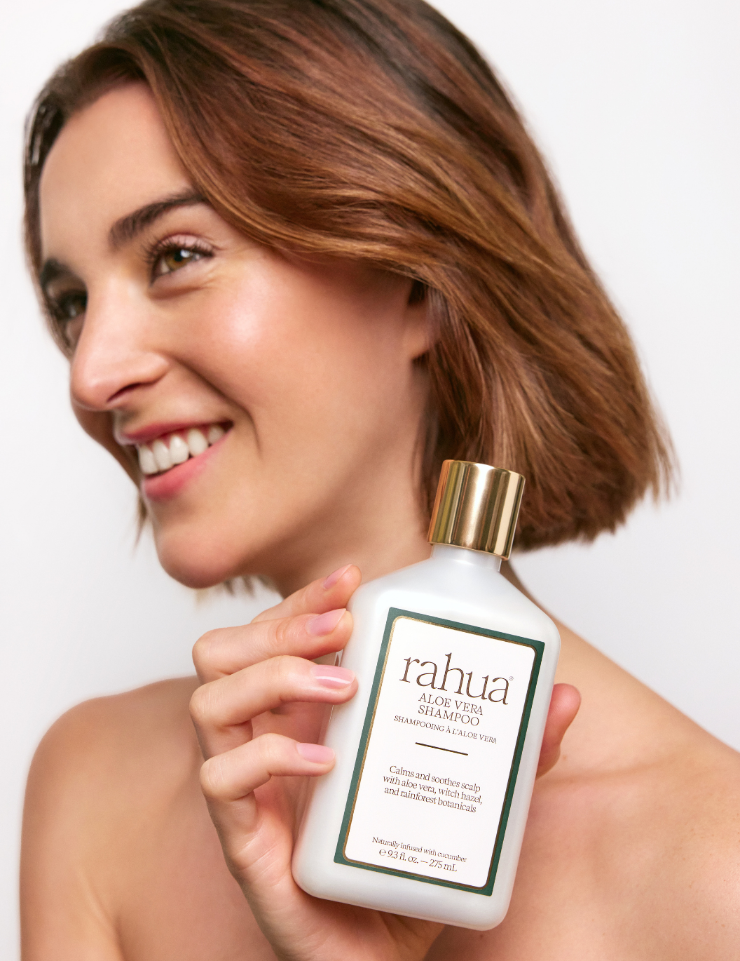 Woman holding a bottle of Rahua Aloe Vera Shampoo against a plain background
