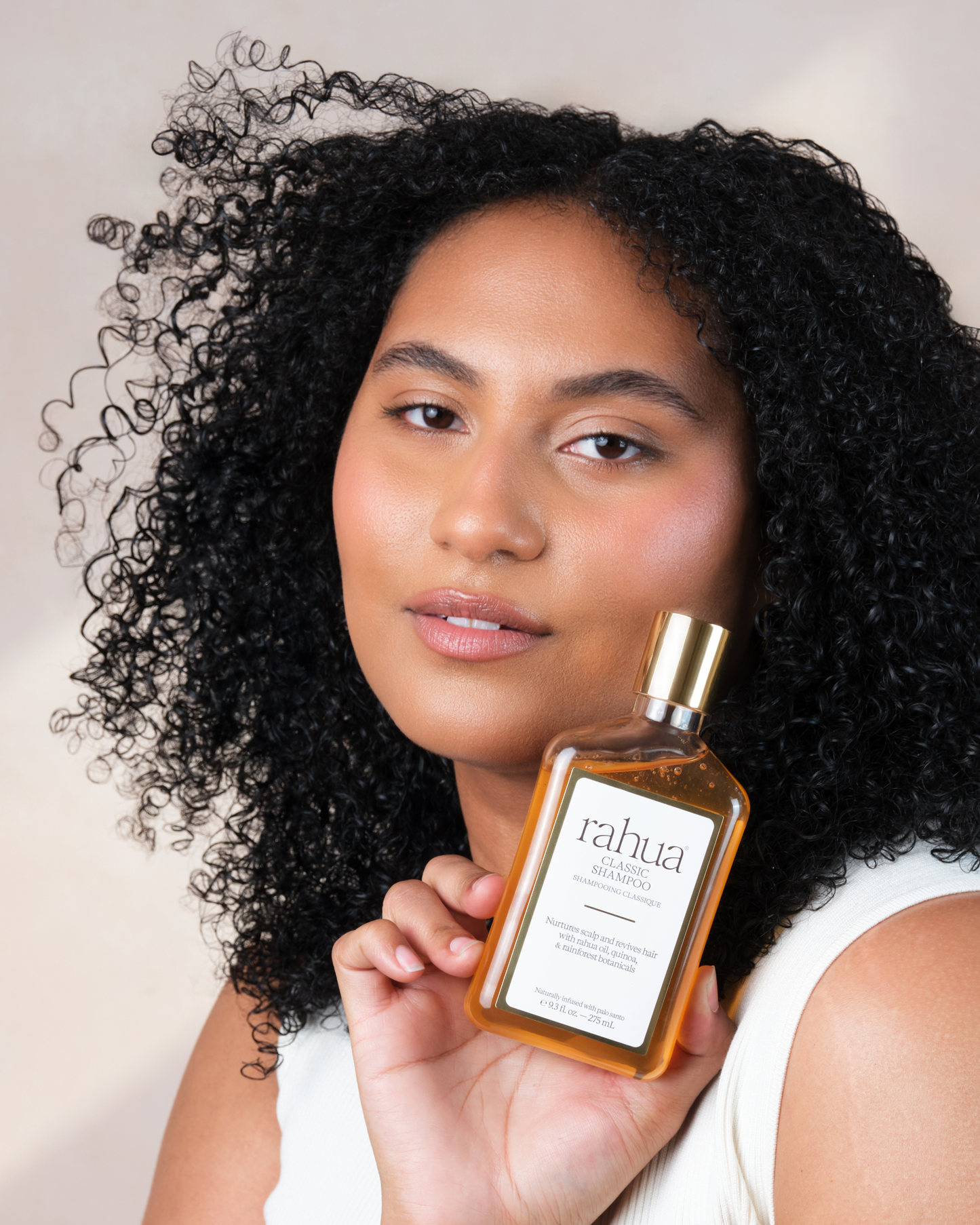 Woman holding a bottle of rahua hair product with a neutral background|variant:93-oz,16-oz,18-oz