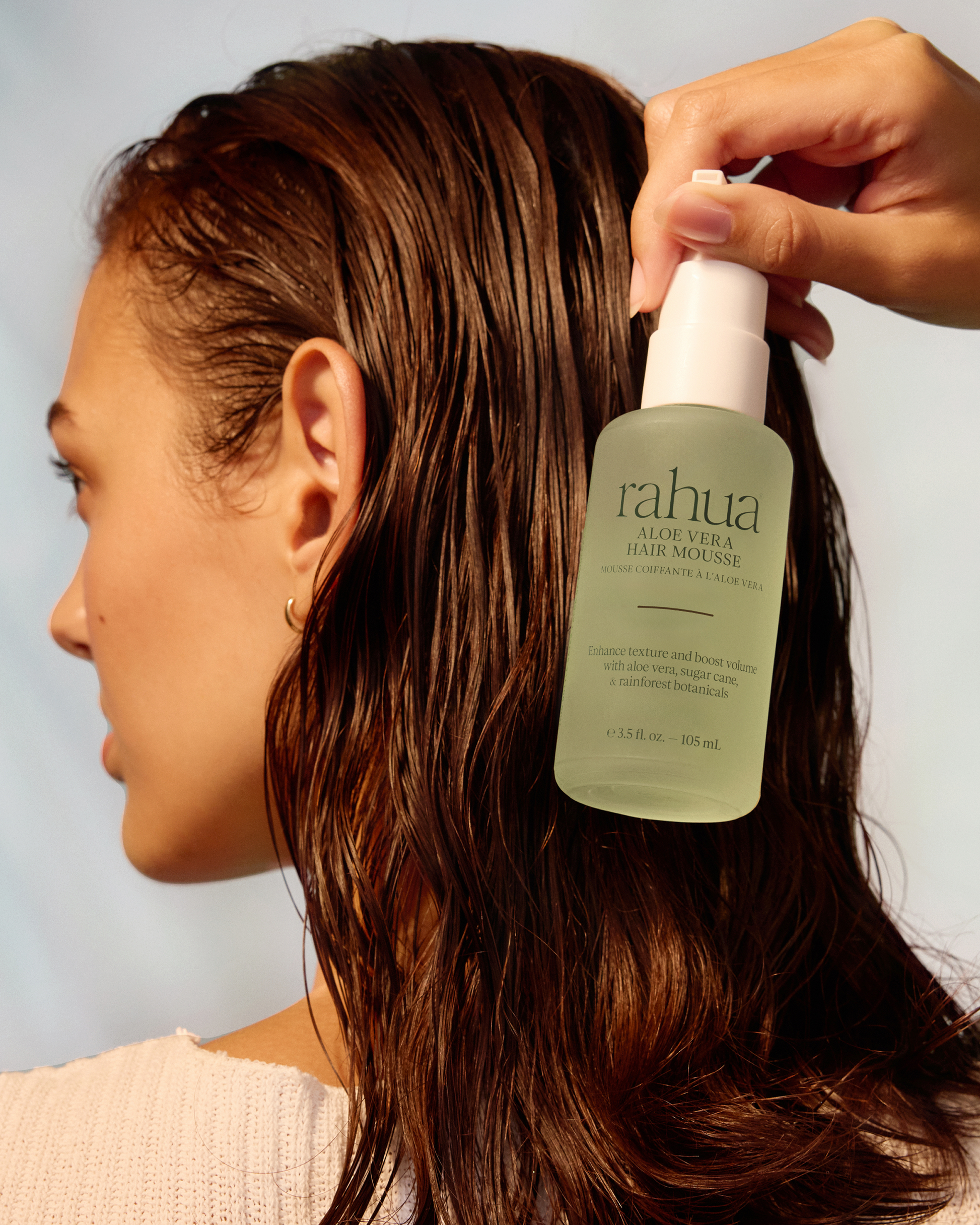 Person applying Rahua aloe vera hair mousse to their hair against a neutral background