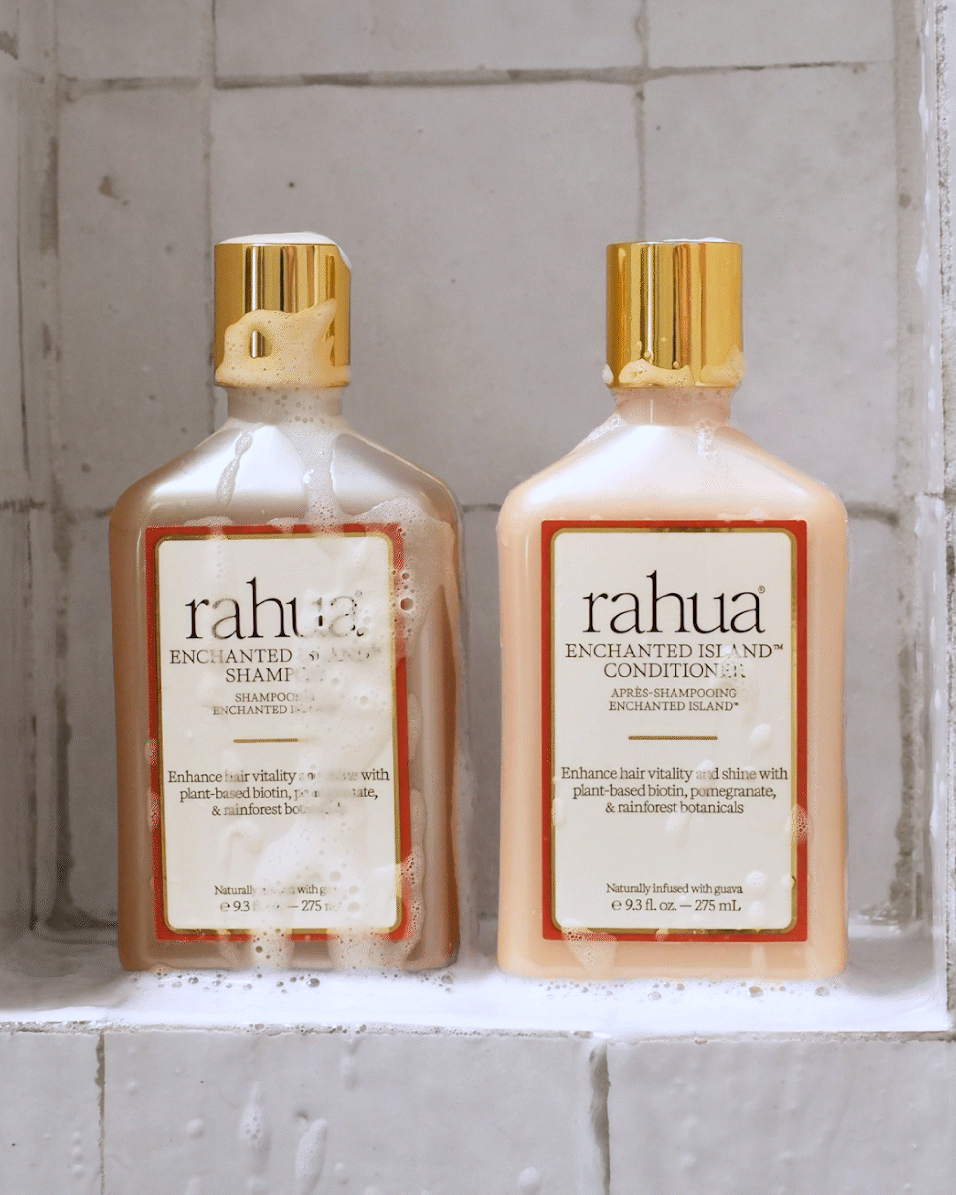 Two bottles of rahua enchanted island shampoo and conditioner on a stone surface with suds on the bottles|variant:93-oz