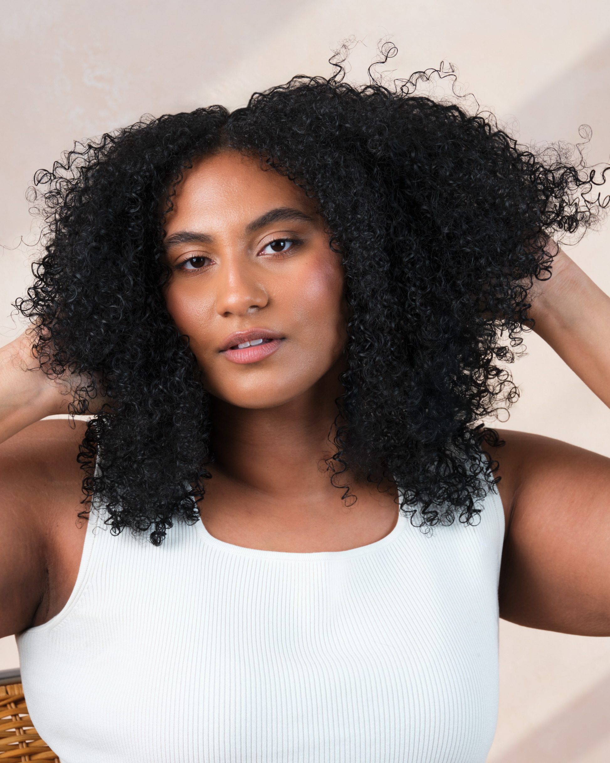 Woman with voluminous curly hair wearing a white tank top against a neutral background|variant:1-oz