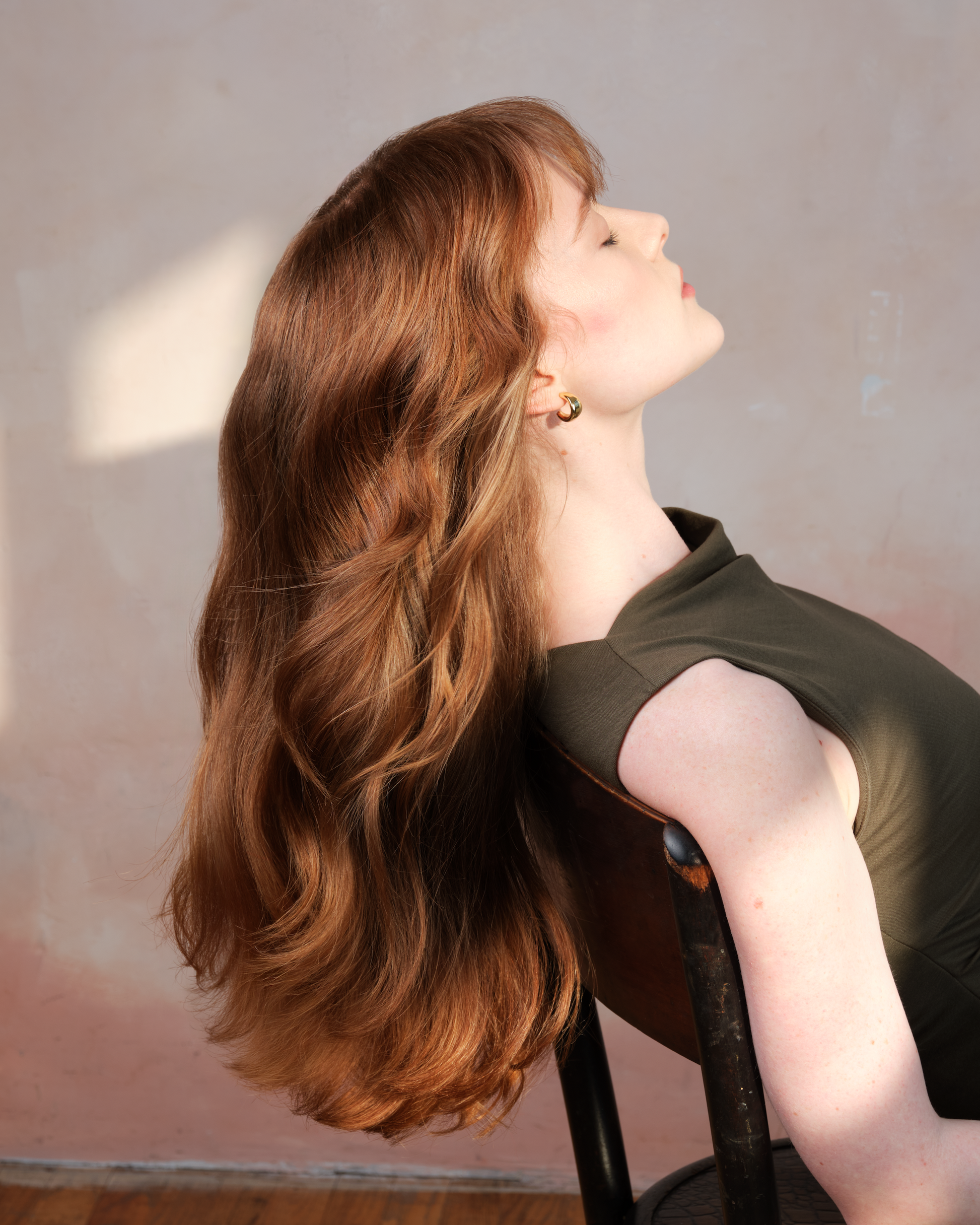 Woman with long wavy hair sitting on a chair against a neutral background|variant:1-oz