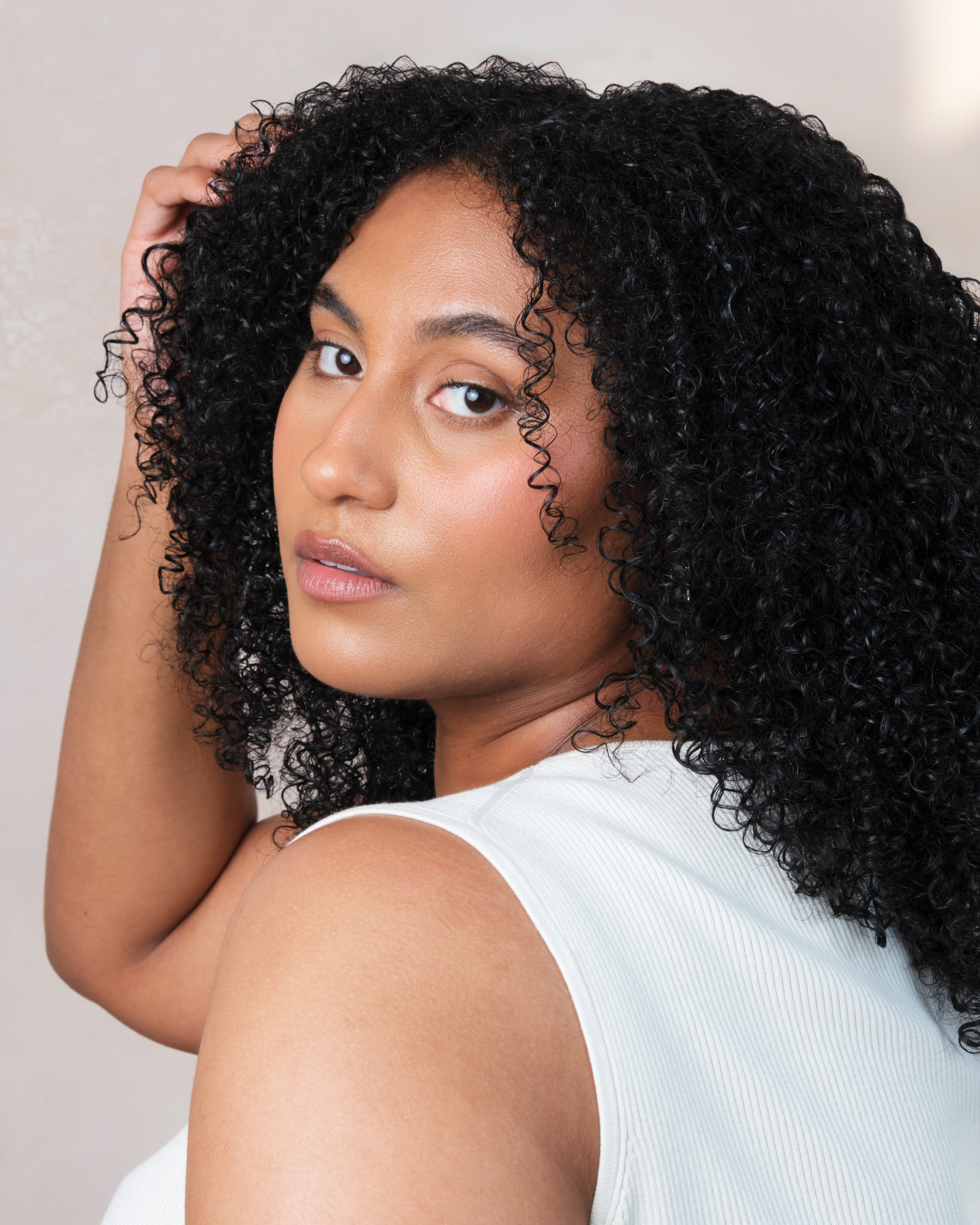 Woman with curly hair looking over her shoulder against a neutral background