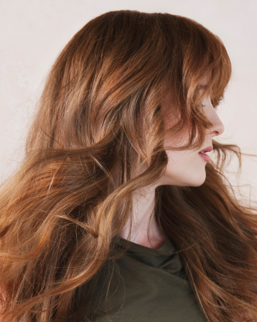 Side profile of a person with wavy red hair against a neutral background