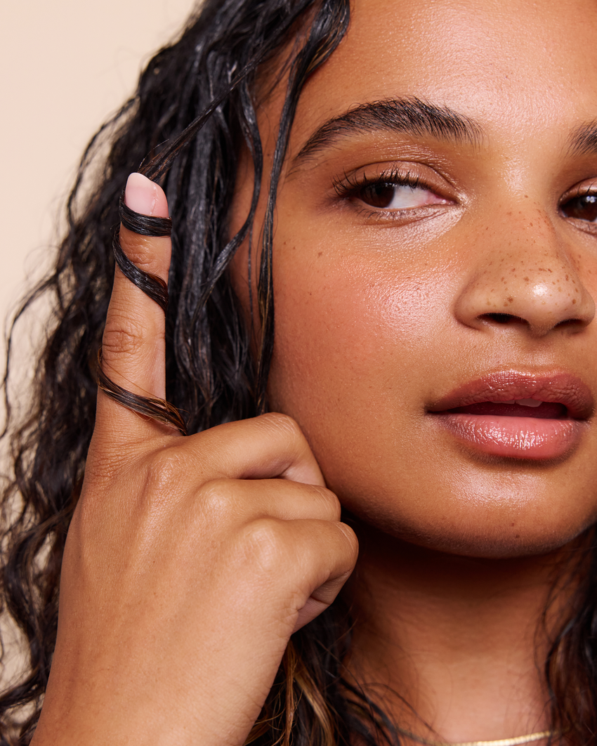 Close-up of a woman with wet hair touching her face against a beige background