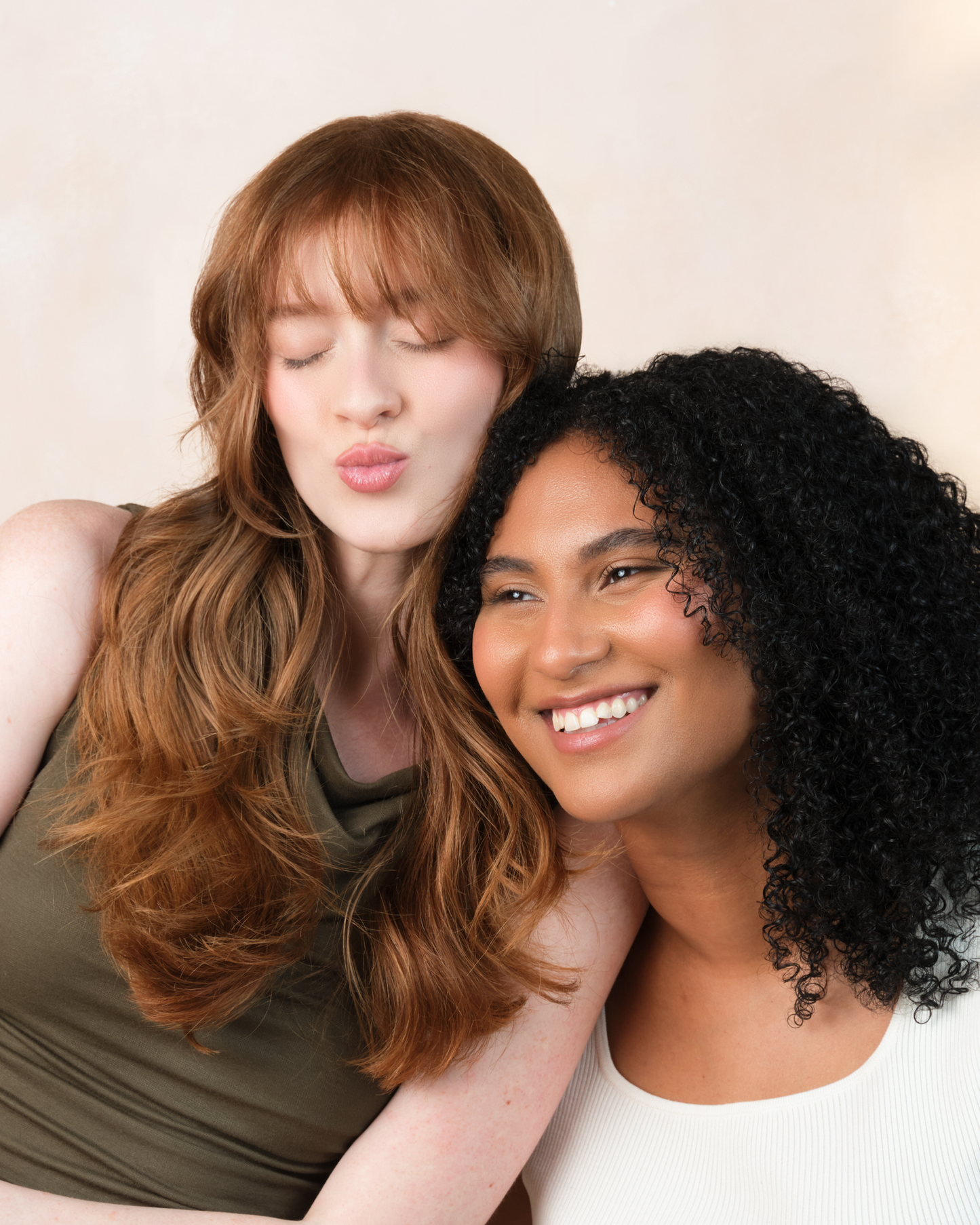 Two women posing closely together with a plain background