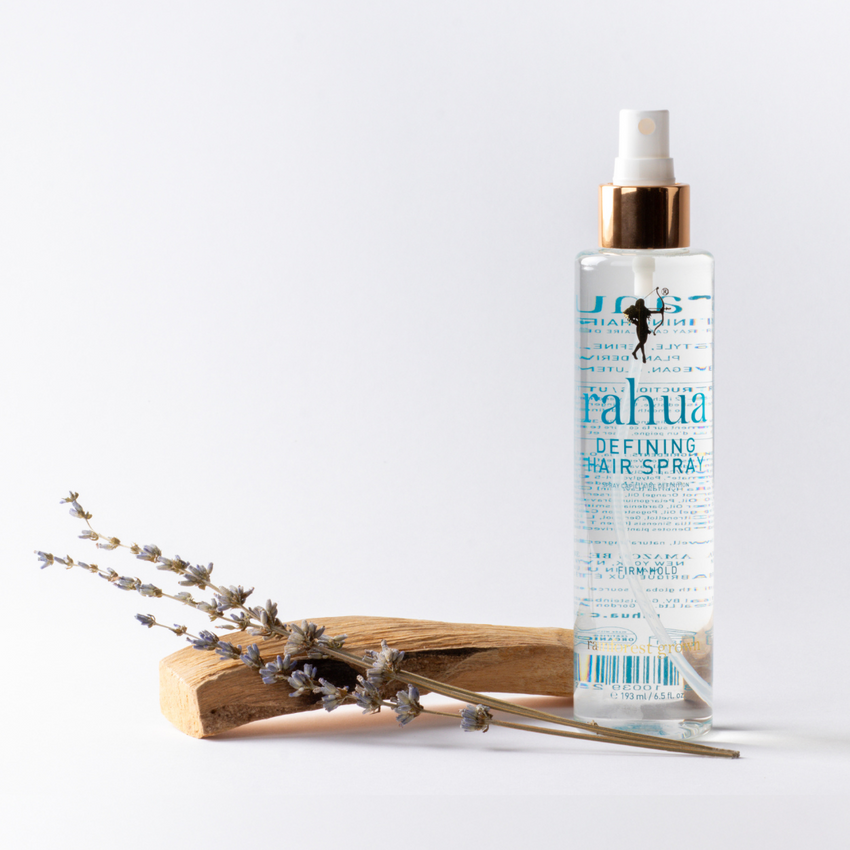 A bottle of Rahua defining hair spray with a white pump and transparent bottle, displaying the light blue liquid inside with wood and flowers