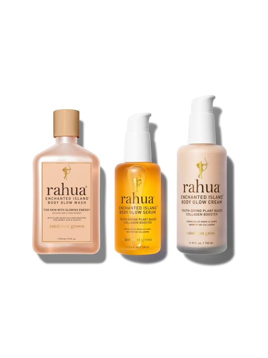 Three products from the Enchanted Island Body Glow Collection including a body glow wash, serum, and cream, each in distinctively shaped bottles with a white and orange color scheme.