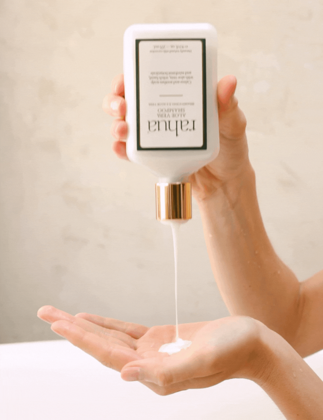 woman dispensing rahua Aloe vera shampoo into hand on plain beige background