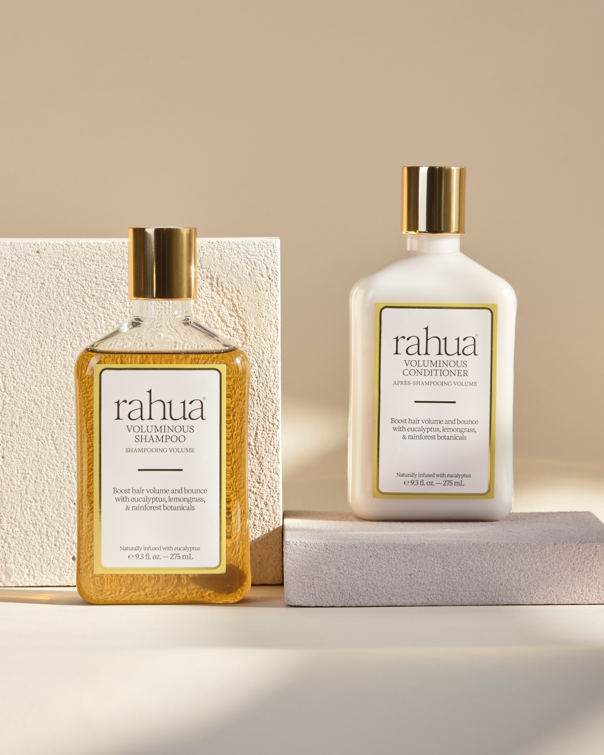 Two bottles of rahua hair care products on a neutral background voluminous shampoo and conditioner sitting on two stone slabs|variant:93-oz