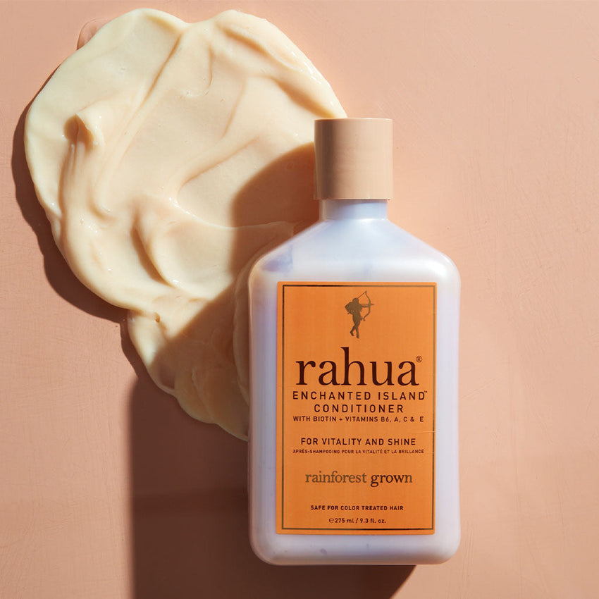 bottle of rahua enchanted island conditioner on an orange background with a dollop of product