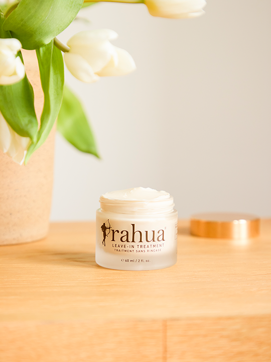 jar of leave in treatment from rahua on a wooden table with tulips in a vase in the background