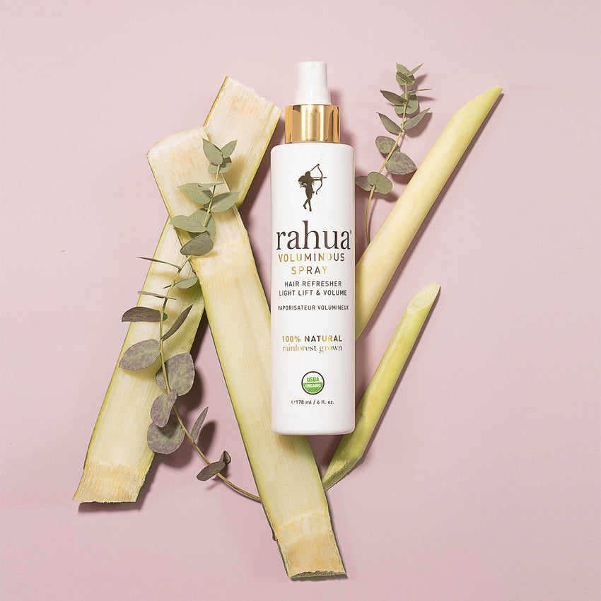 Rahua Voluminous Spray bottle with Lemongrass, Sugar cane, and Eucalyptus on a plain pink background