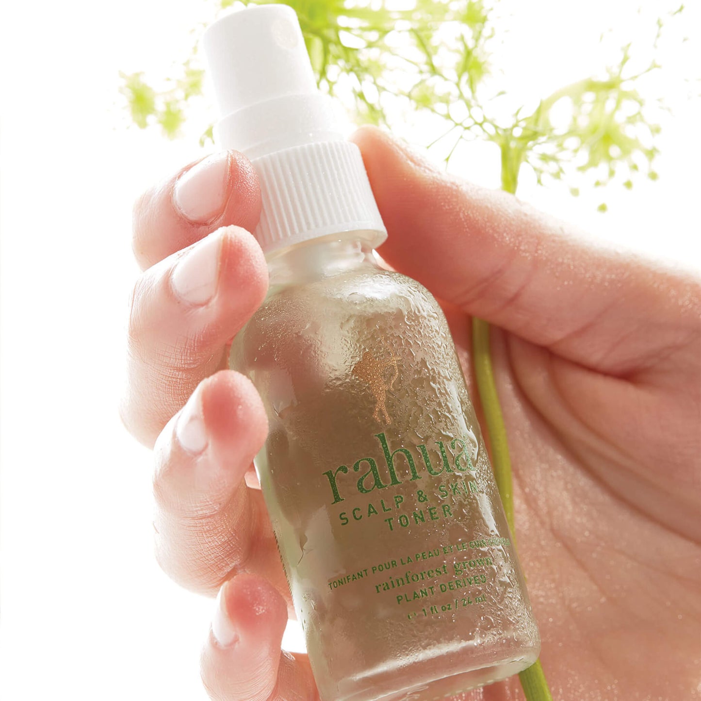 Rahua Scalp and Skin Toner in hand with plant