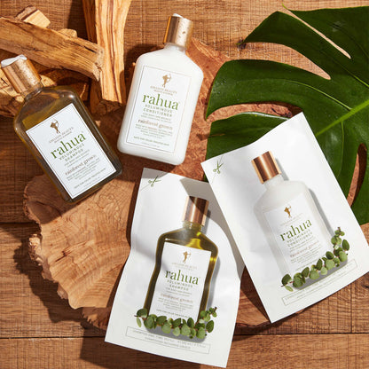 Rahua Voluminous shampoo and conditioner refill and bottles are kept on a wooden plank with palo santo sticks and carnauba leaf